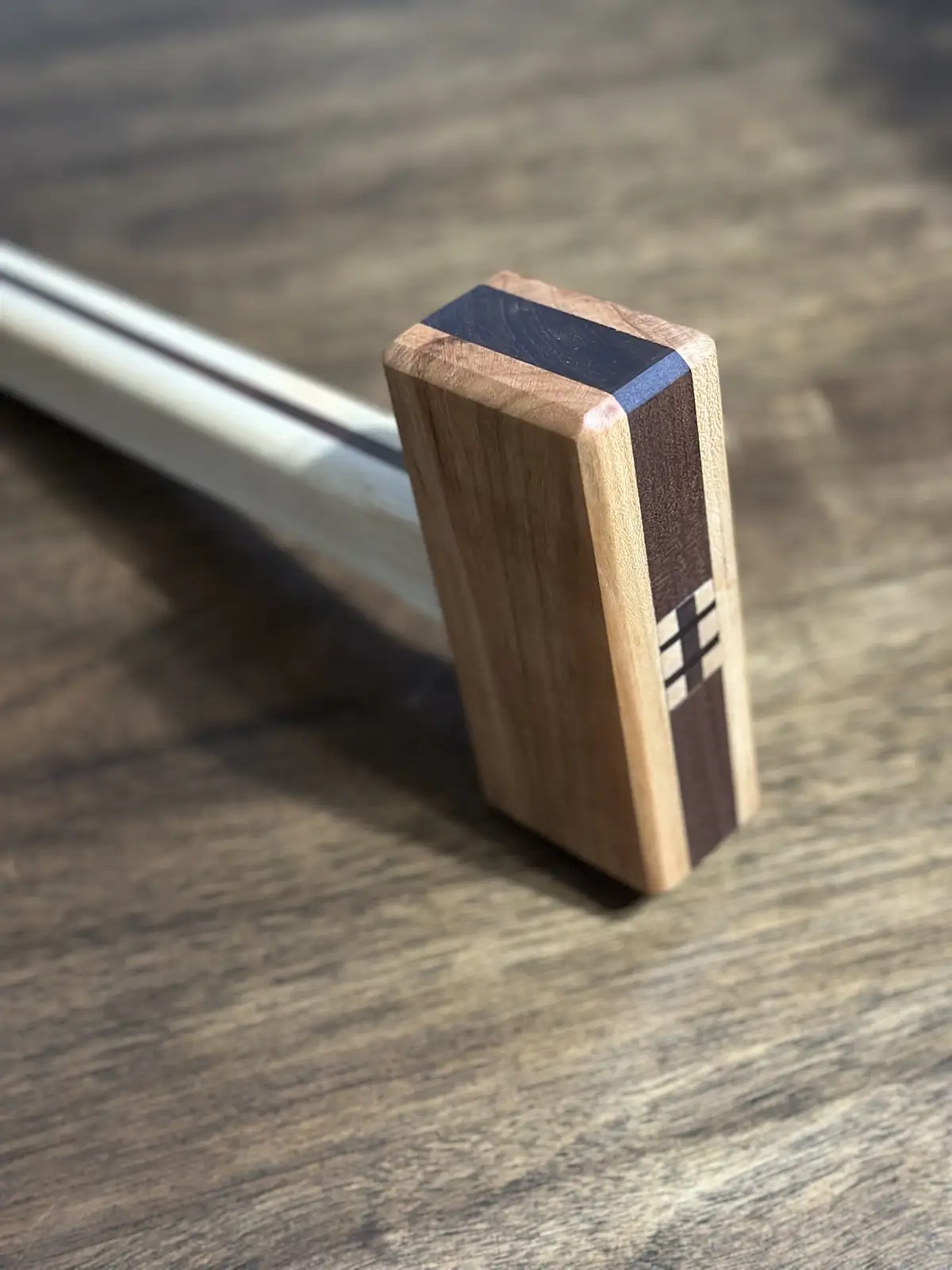 A close-up photo shows a small, rectangular wooden block standing upright on a wooden surface, designed to resemble a house…
