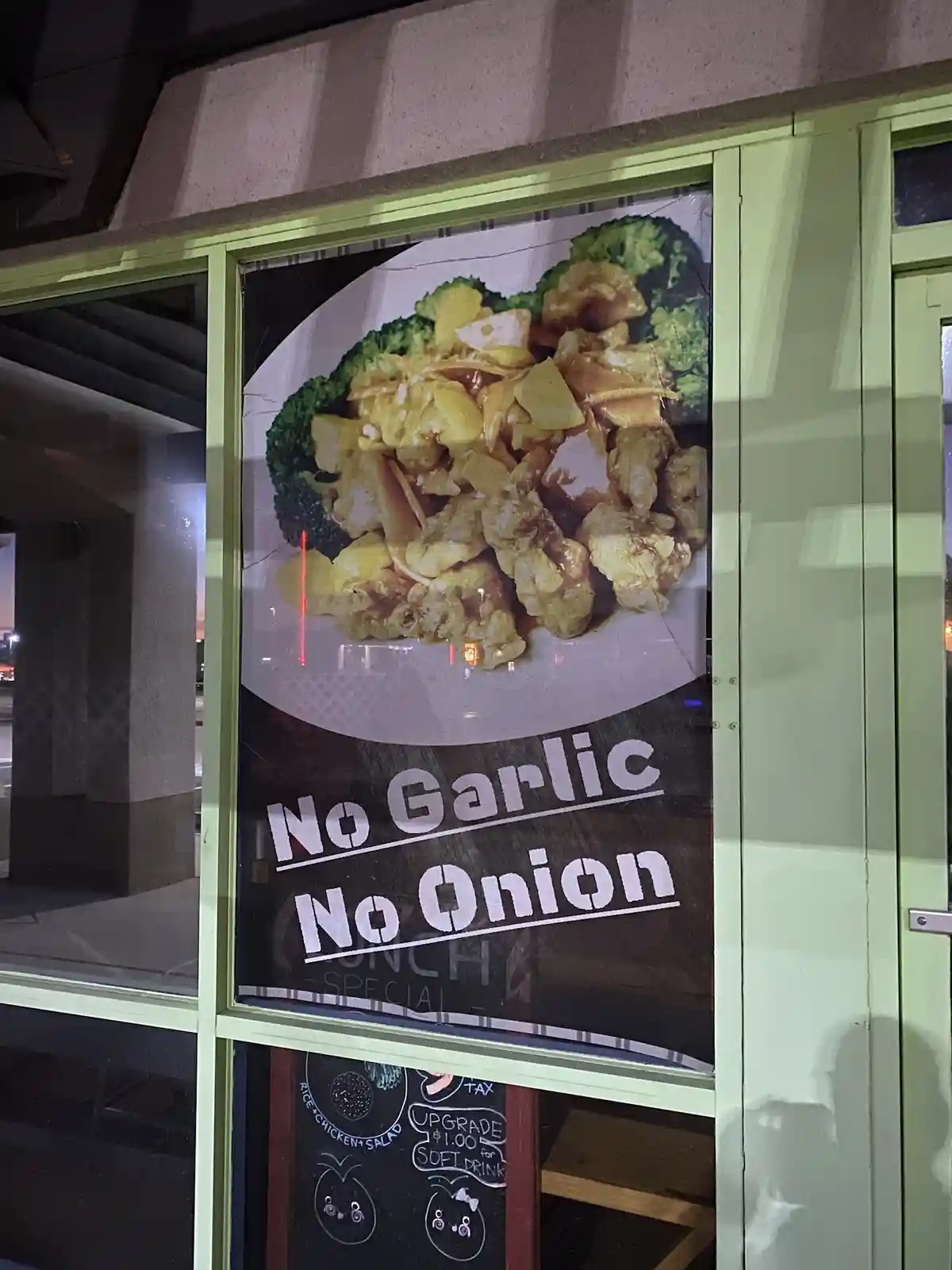 A restaurant window poster shows a photo of a plate of chicken with broccoli and pineapple. Overlaid in large white…