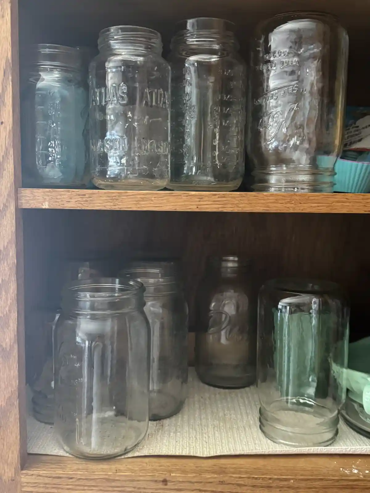 A wooden shelf holds multiple empty glass mason jars of various sizes and brands, some dusty and dirty, arranged on two…