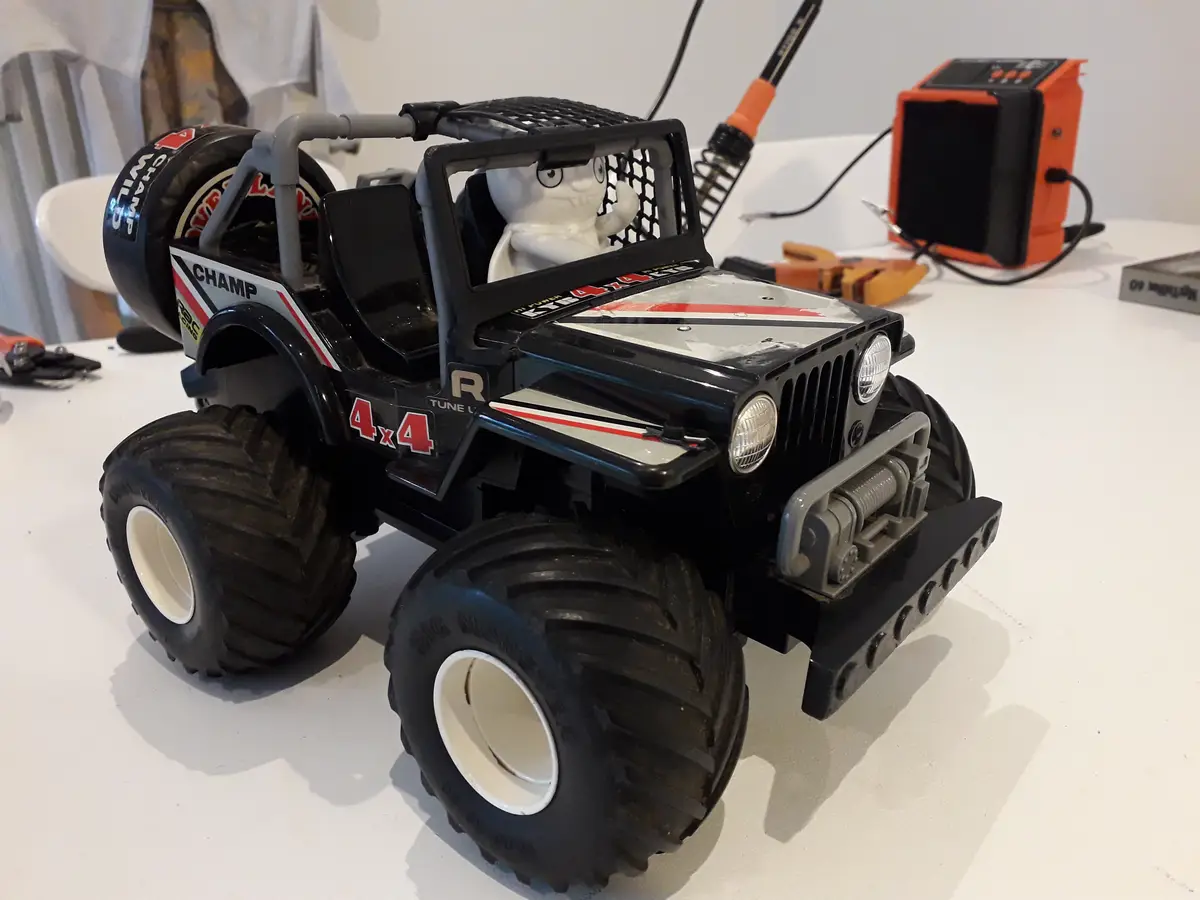 A black toy monster truck with large tires and a white cartoon character figure in the driver's seat sits on a white table…