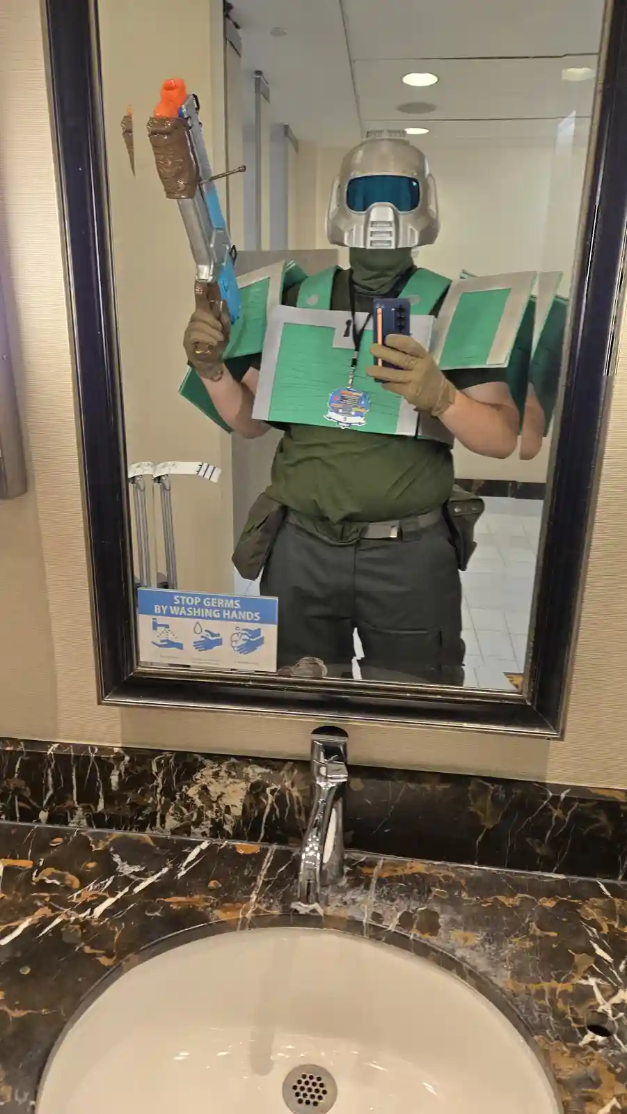 A person in a full-body costume resembling a green and silver robot or soldier, complete with a helmet, gloves, and chest…