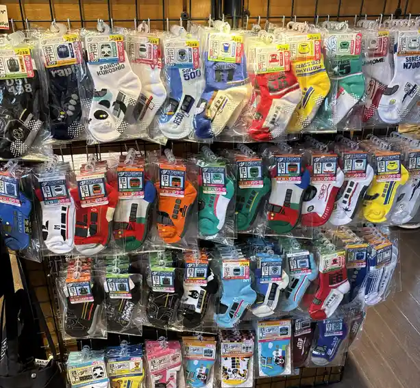 A retail display of colorful, individually packaged children's socks featuring various Japanese train models and characters…