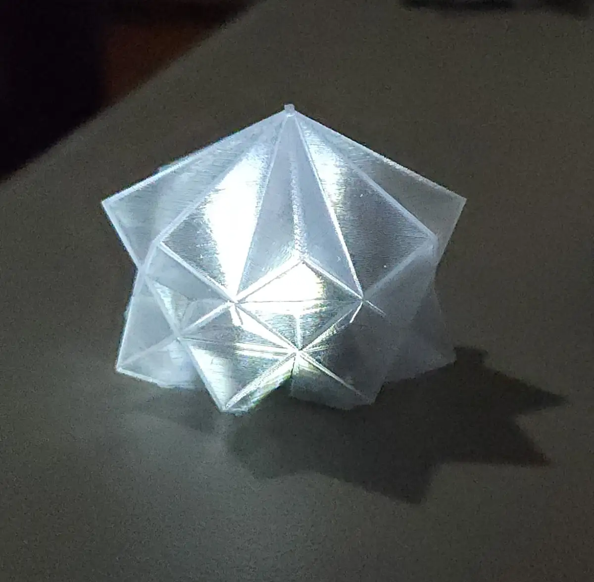 A translucent, 3d-printed geometric star-shaped object sits on a dark surface, glowing from within and casting a star-shaped…