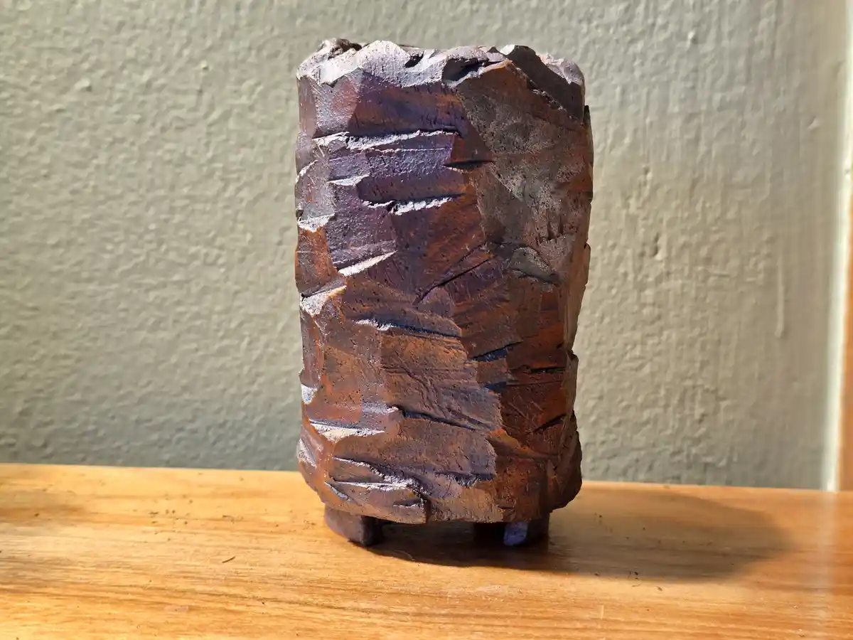 A roughly carved wooden object, resembling a small, cylindrical sculpture with visible tool marks and a rustic finish, sits…