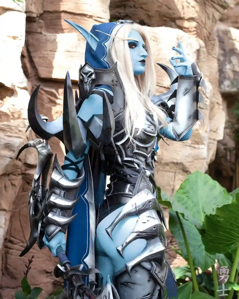 A person in detailed blue-skinned fantasy armor with pointed ears and ornate silver and black plate, standing outdoors near…