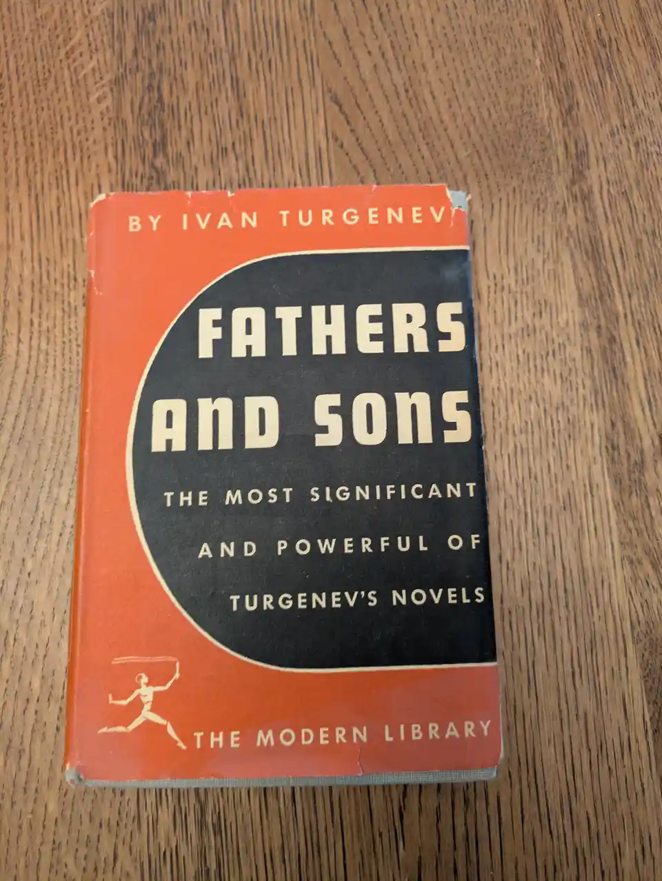 A vintage orange and black book cover for Ivan Turgenev's 'Fathers and Sons' from The Modern Library, resting on a wooden…