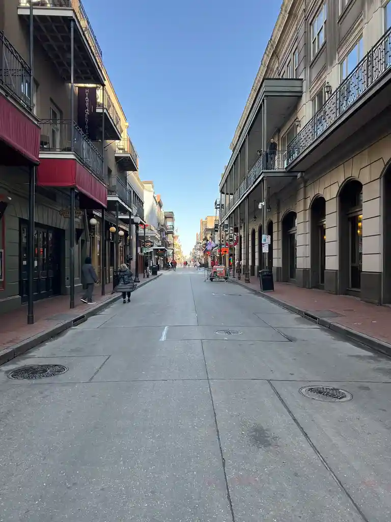 A low-angle photo of a nearly empty, wide street lined with historic buildings featuring wrought-iron balconies, under a…