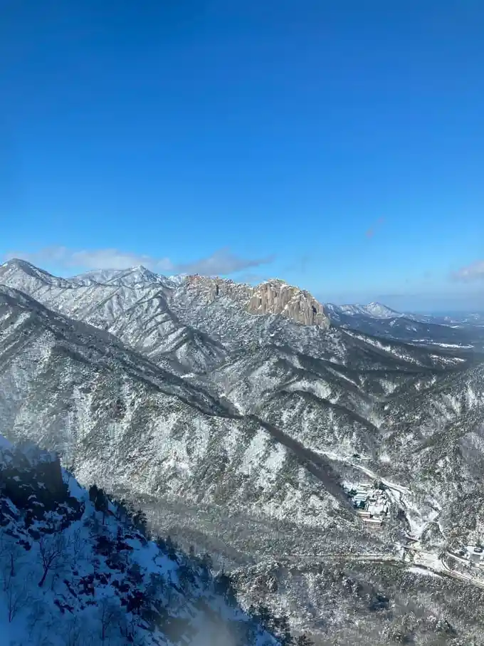 A scenic, high-angle photograph of snow-covered mountains under a clear blue sky, with a small village nestled in the valley…