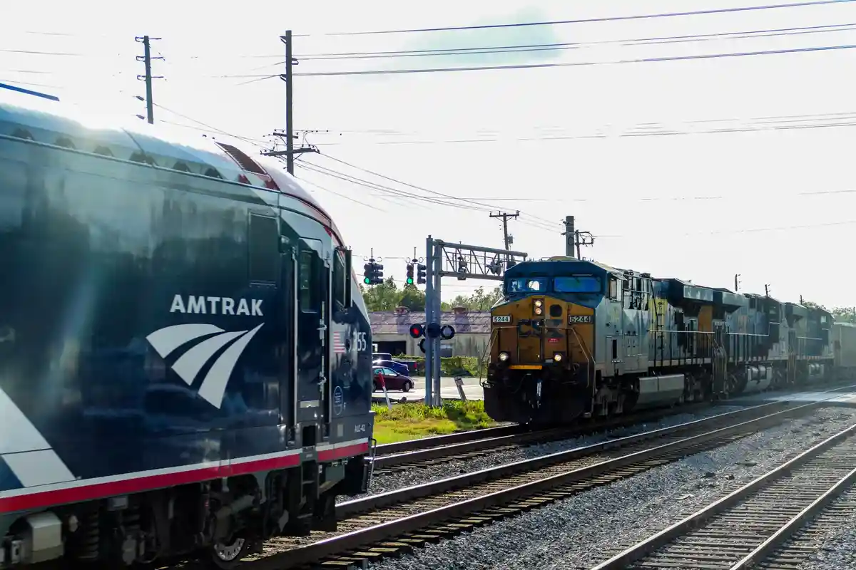 Two trains are on parallel tracks, one Amtrak passenger train on the left and a CSX freight train on the right, with traffic…