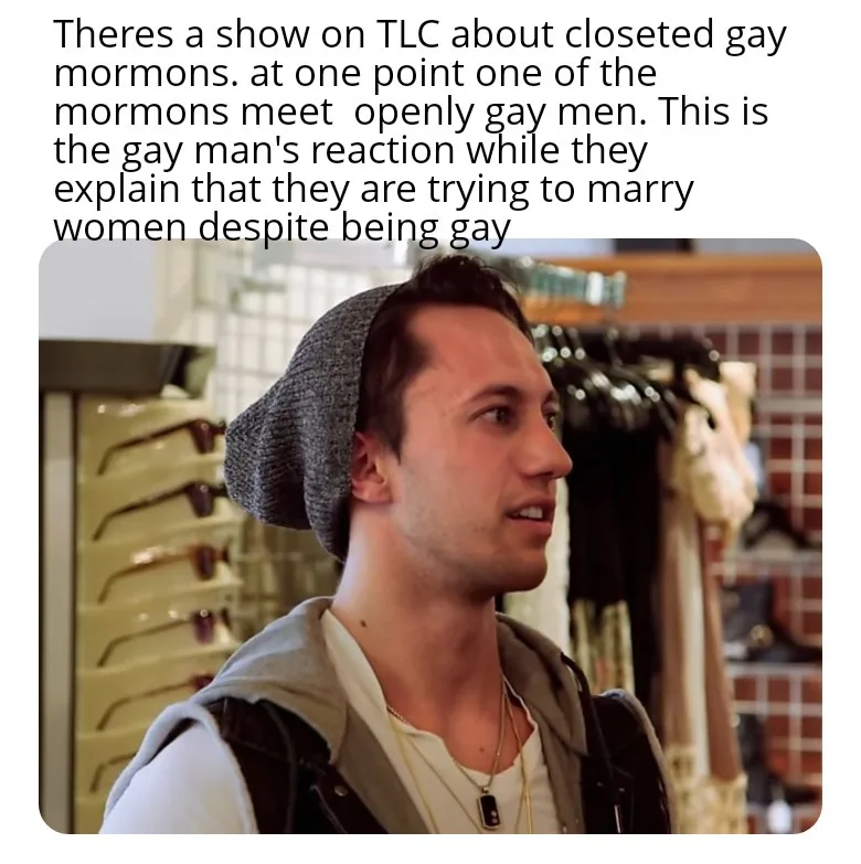 A man wearing a grey beanie, a white t-shirt, and a grey hoodie looks off to the side with a surprised expression. The…