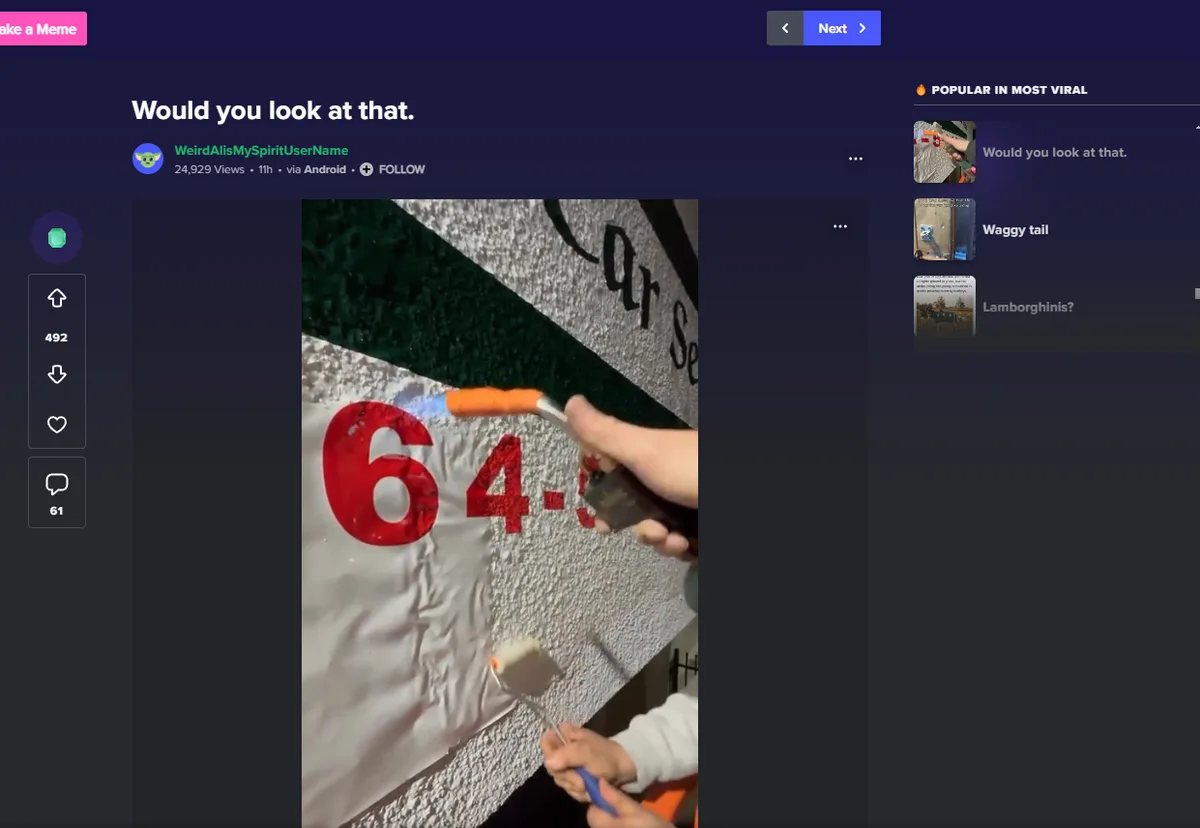 A person is painting large red numbers '64-' onto a white textured surface with a paint roller, while another hand holds a…