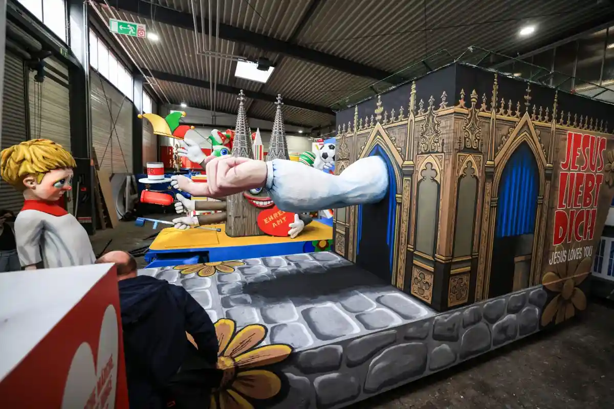 A large, colorful parade float depicts a cartoonish scene with a giant hand emerging from a gothic-style church facade…