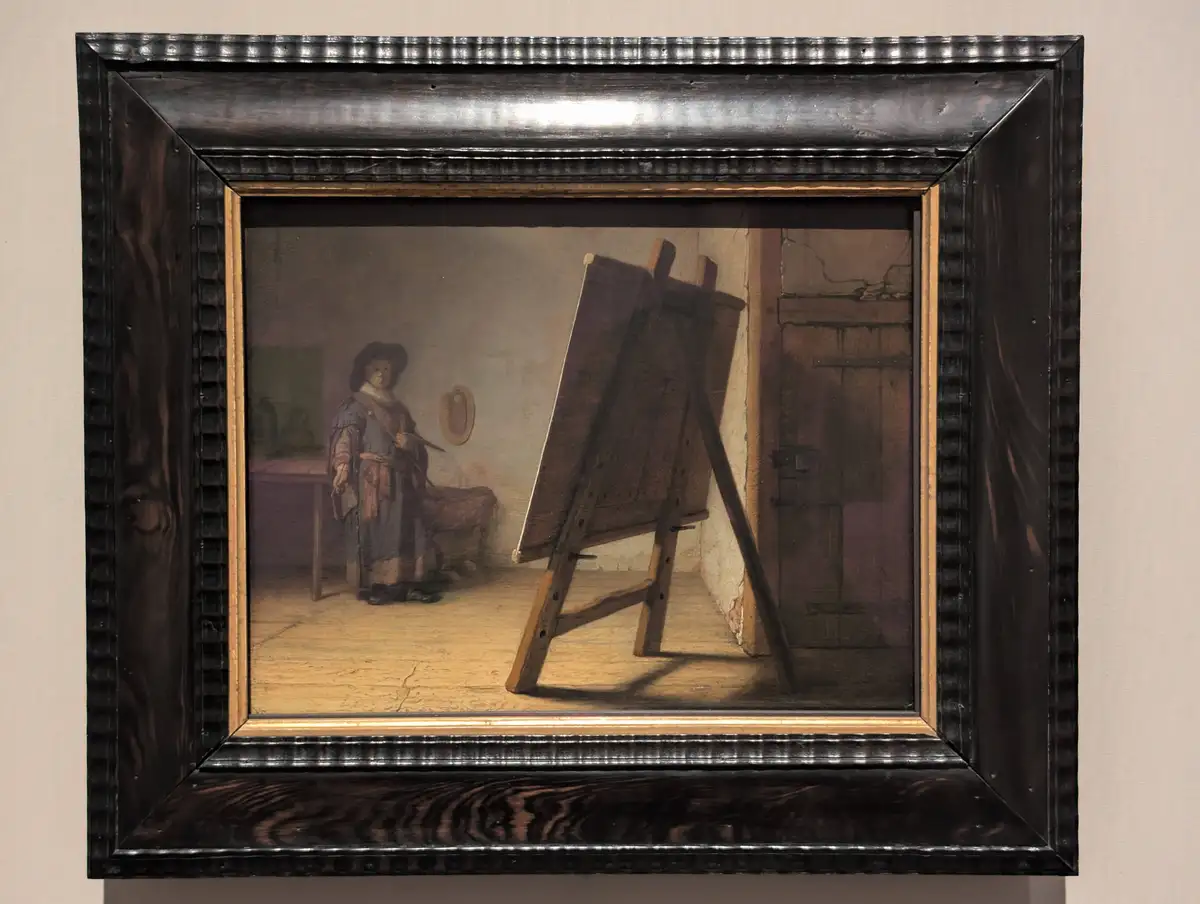 A framed painting depicts a person in historical clothing standing in a room with a wooden easel, seemingly painting…