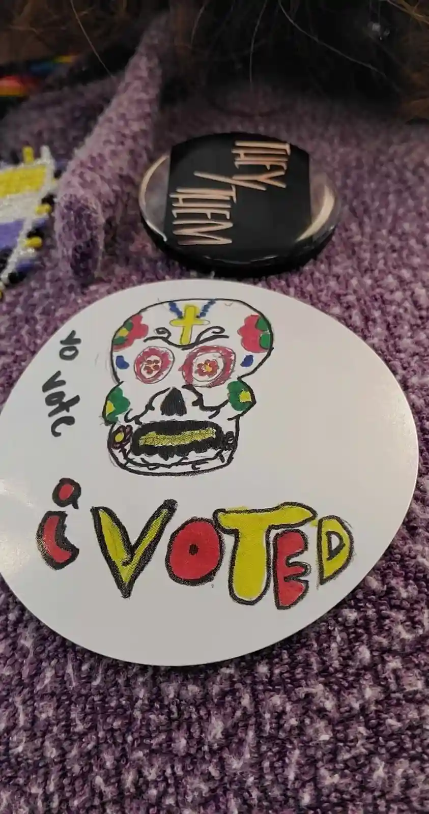 A hand-drawn, colorful sugar skull sticker with 'i voted' written below it and 'to vote' written vertically to the left…