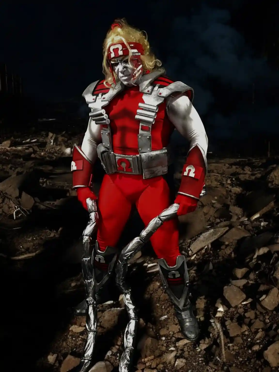 A person in a red and silver costume with a blonde wig and an omega symbol on their headband, chest, arms, and legs stands…