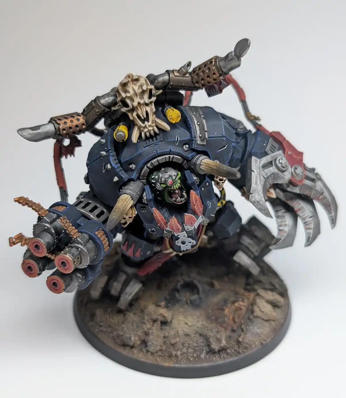 A heavily armored, green-skinned Ork warboss miniature from Warhammer 40,000, featuring a skull-topped weapon, multiple…