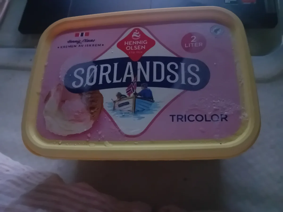 A close-up photo of a yellow plastic tub of Hennig Olsen Sørlandsis Tricolor ice cream, showing the label with a boat…