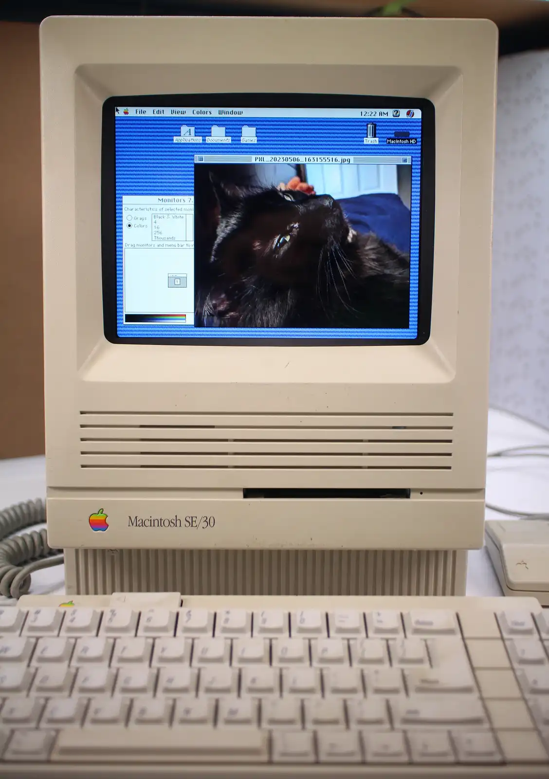 A vintage beige Apple Macintosh SE/30 computer with its screen displaying an old-style Mac OS interface. The screen shows a…