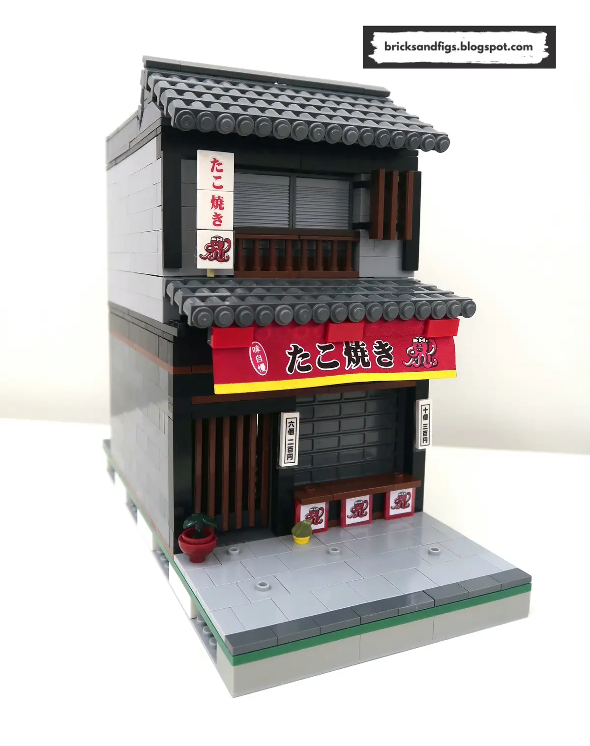 A detailed LEGO model of a two-story Japanese takoyaki restaurant with traditional architecture, red signage displaying…