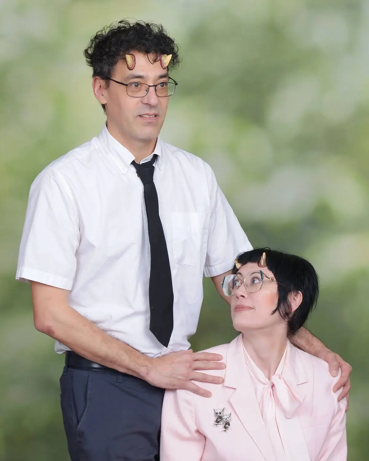 A man and woman pose together in a photo, both wearing small golden devil horns on their heads. The man, in a white shirt…