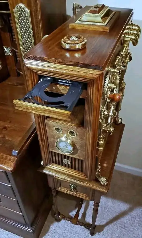 a wooden cabinet with brass fittings and exposed gears, resembling a vintage machine, has a drawer pulled open revealing a…