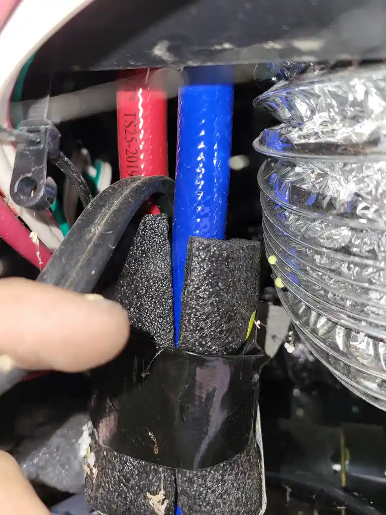 A close-up photo shows a person's finger pointing at a blue electrical wire inside a car's engine bay, surrounded by other…
