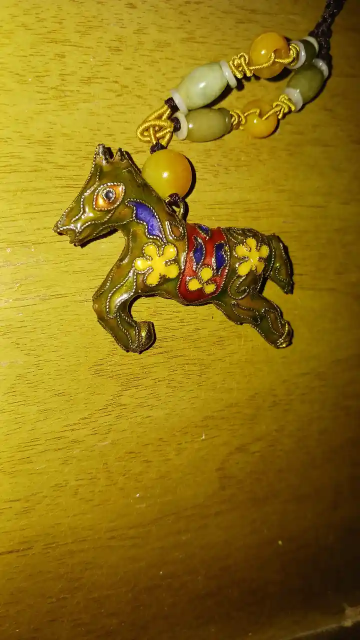 A close-up photo shows a colorful, ornate horse-shaped pendant with enamel detailing in green, red, blue, and yellow…