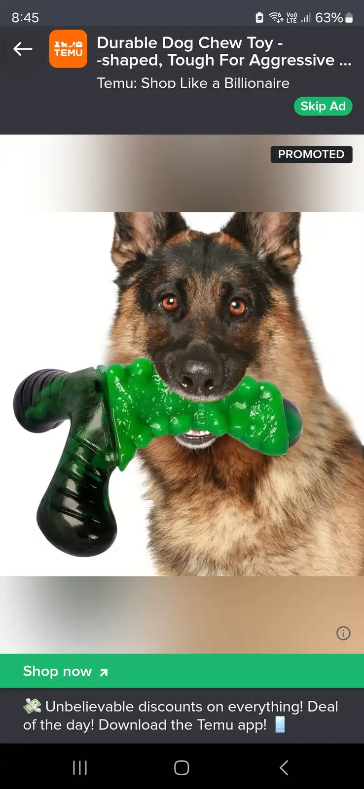 A German Shepherd dog is shown holding a green, bone-shaped chew toy in its mouth against a white background. The image is…