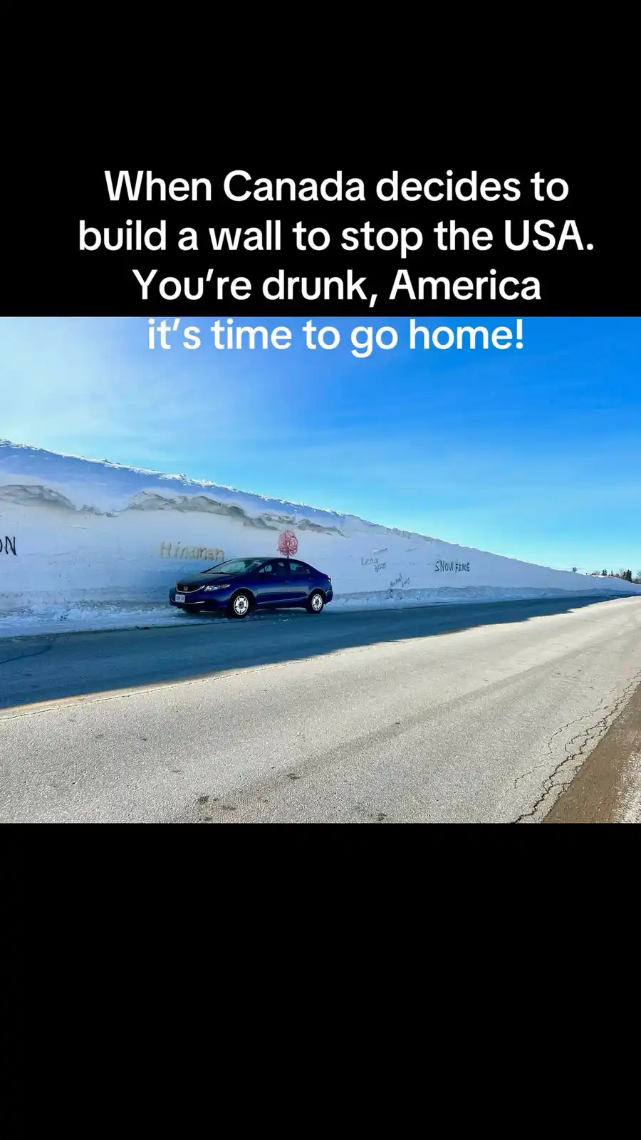 A blue car drives along a road next to an extremely tall, snow-covered barrier that resembles a wall. The sky is clear blue…
