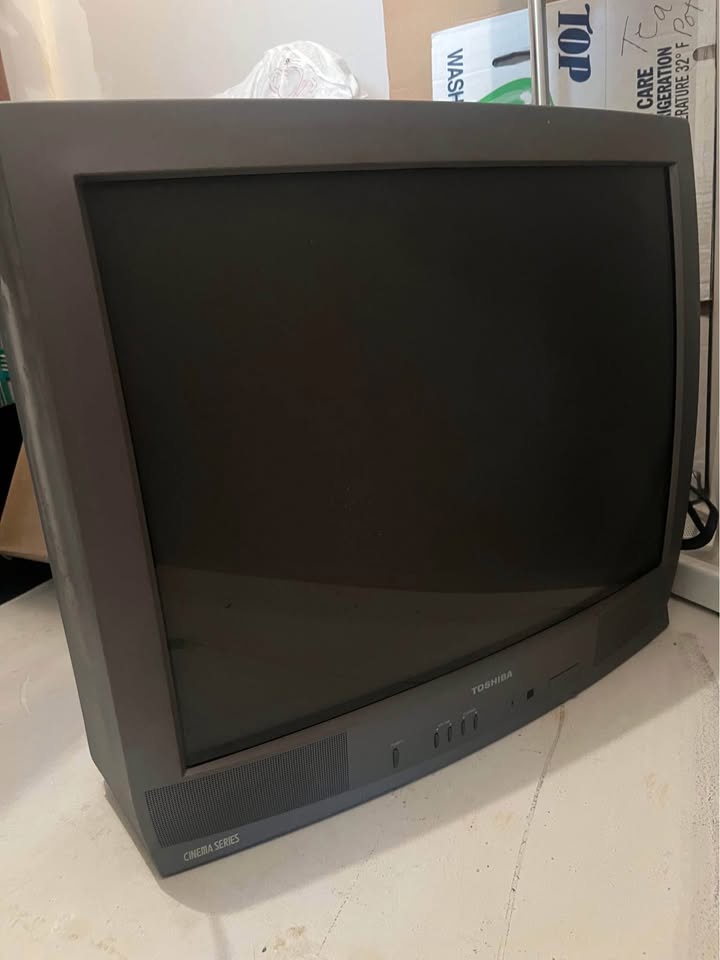 A dark, turned-off, bulky Toshiba CRT television sits on a white surface, with the brand name and 'Cinema Series' visible on…