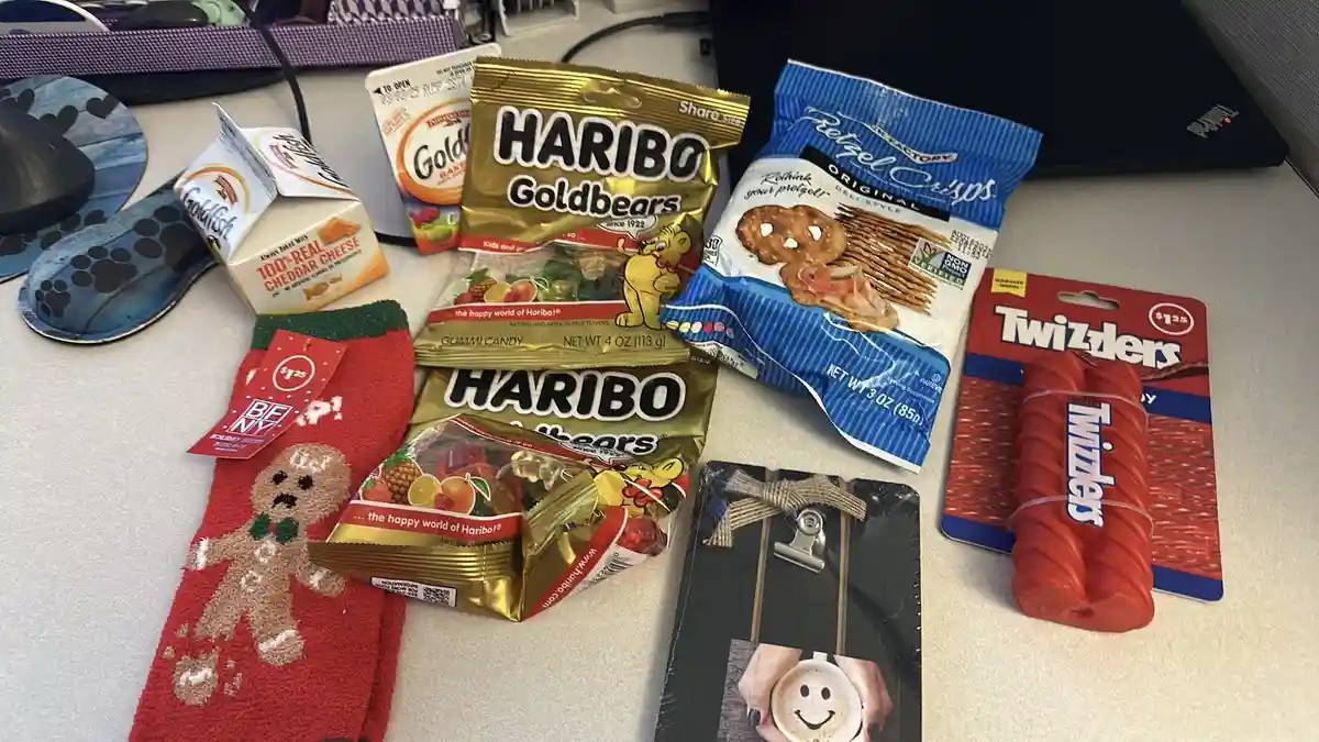 A desk is covered with various snack items including Haribo Goldbears, Twizzlers, Pretzel Crisps, Goldfish crackers, and a…