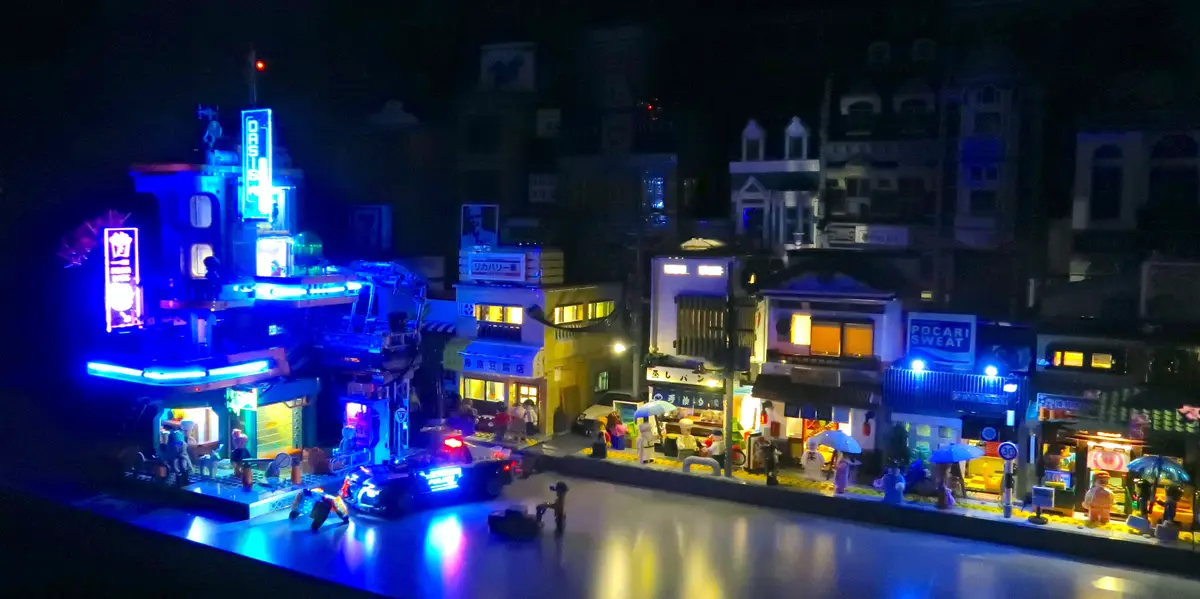 a detailed lego diorama of a japanese city street at night, illuminated by vibrant neon signs and streetlights, featuring…