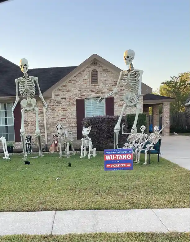 A front yard decorated for Halloween features multiple large skeleton figures, including two standing tall and several…