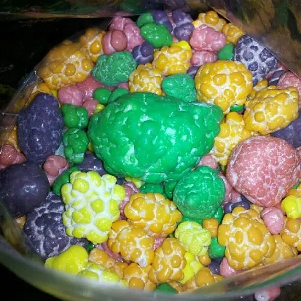 a close-up photo of colorful, brain-shaped candies in a clear plastic bag, with one large green brain-shaped candy…