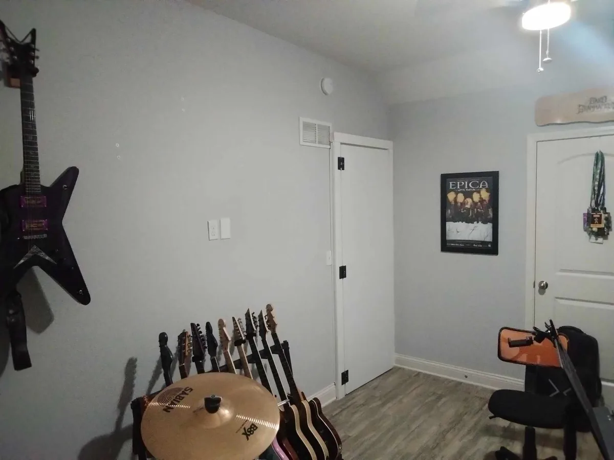 A room filled with musical instruments including multiple guitars on stands, a large Sabian cymbal, and a hanging guitar on…