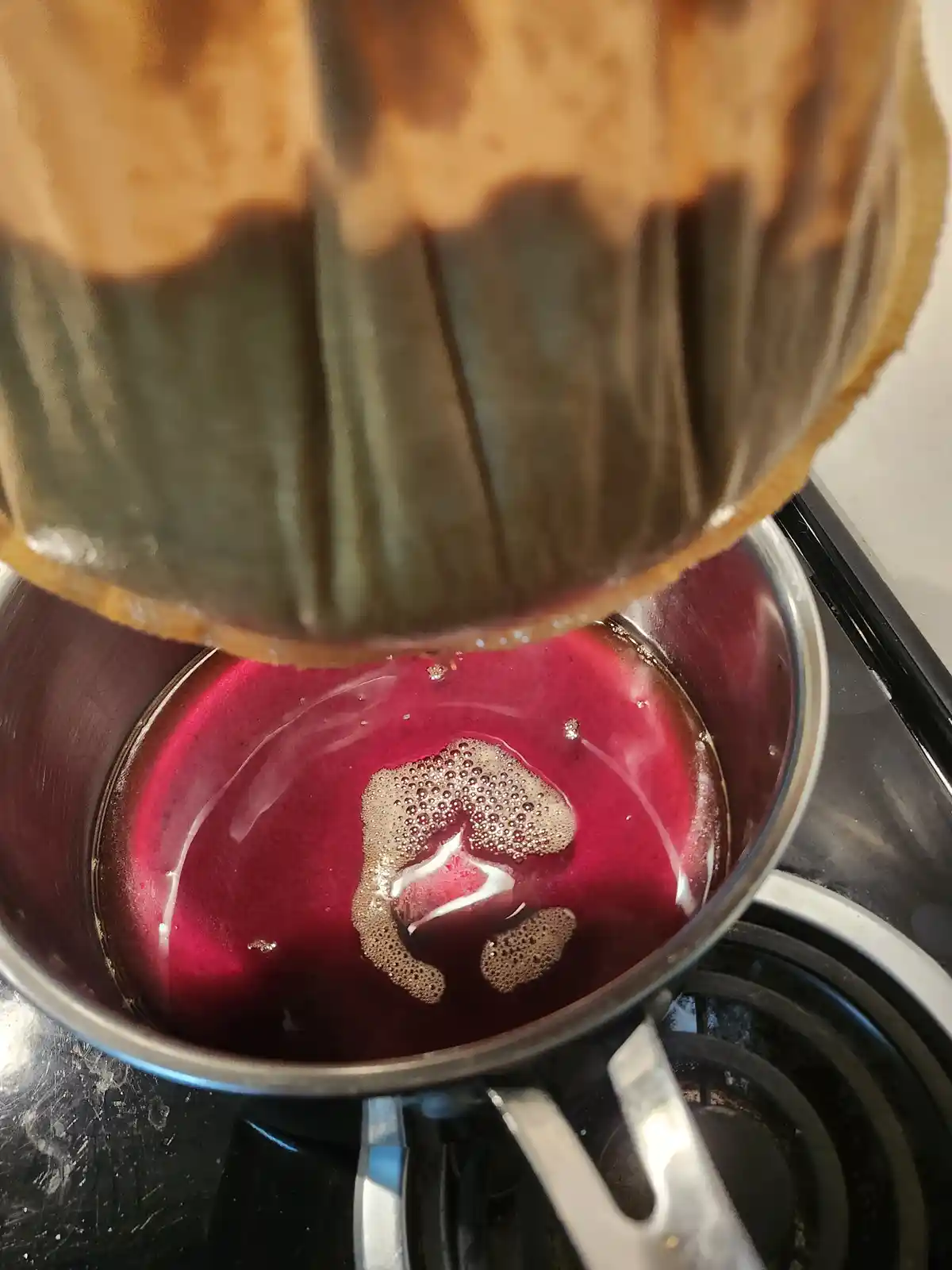 A close-up photo shows a bundt cake being inverted over a saucepan filled with a dark red liquid, which has a small, foamy…