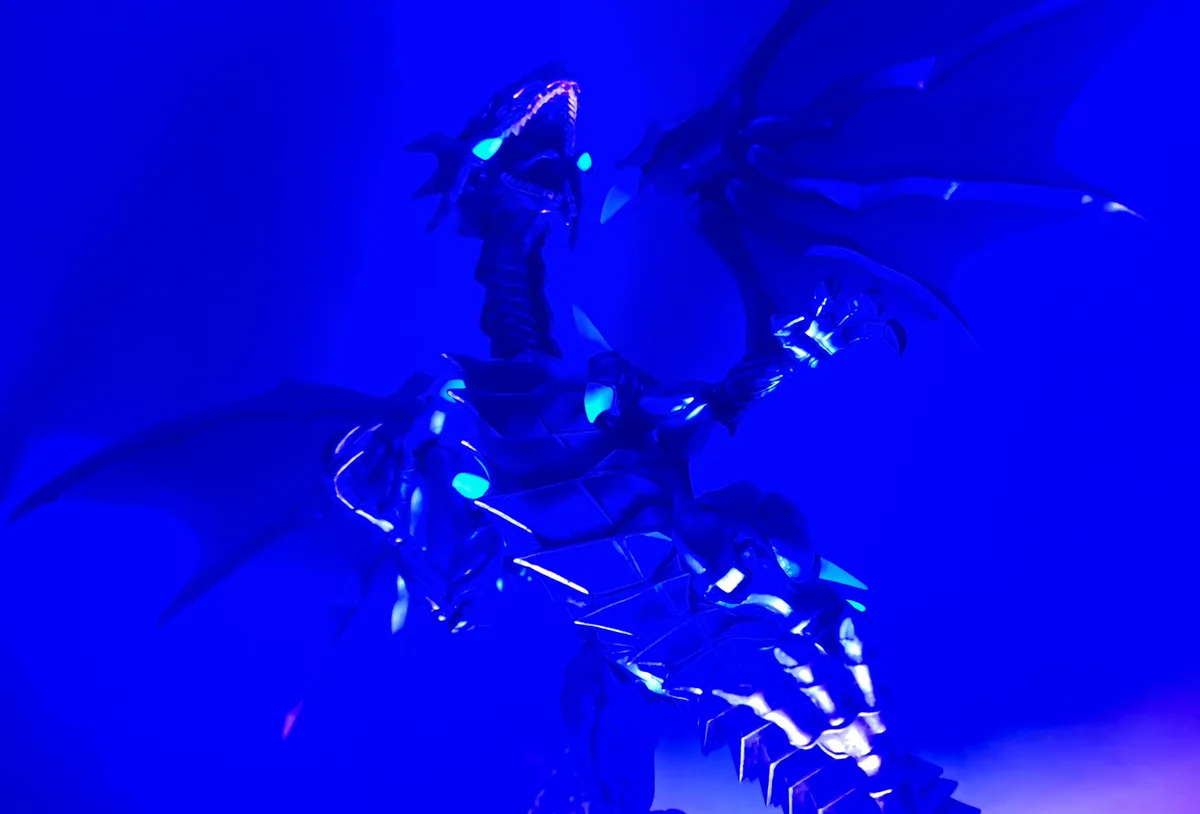 A menacing, stylized dragon figurine with glowing cyan eyes and sharp teeth is posed against a solid blue background, its…