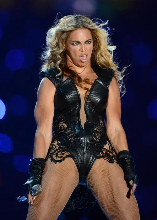 Beyoncé Knowles performs on stage in a black leather and lace bodysuit with fishnet stockings and black gloves, holding a…