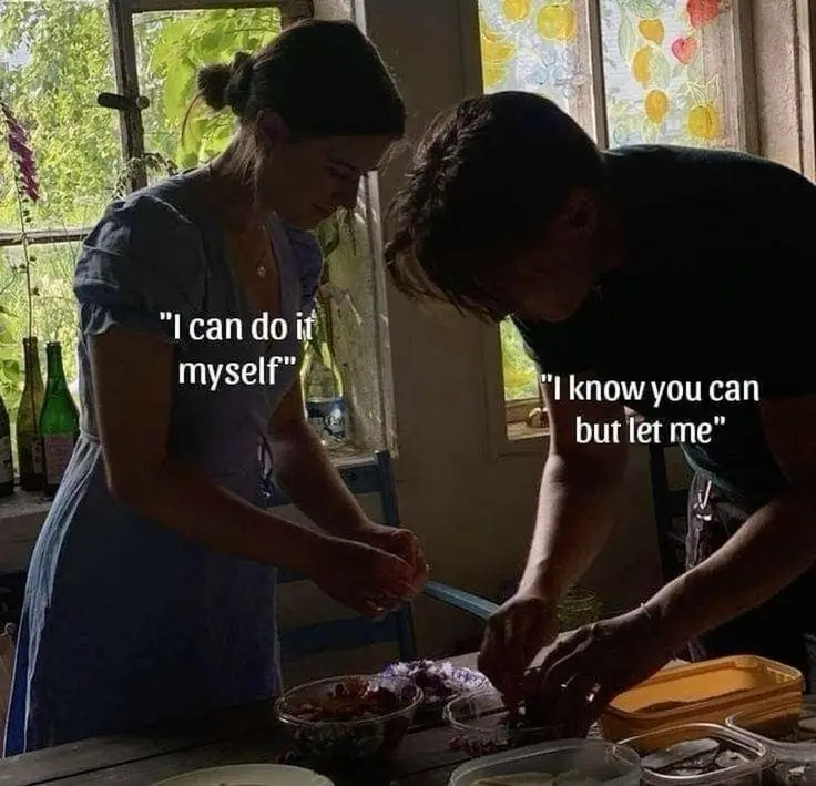 Two people are standing at a kitchen counter preparing food together. The person on the left, wearing a blue dress, has text…