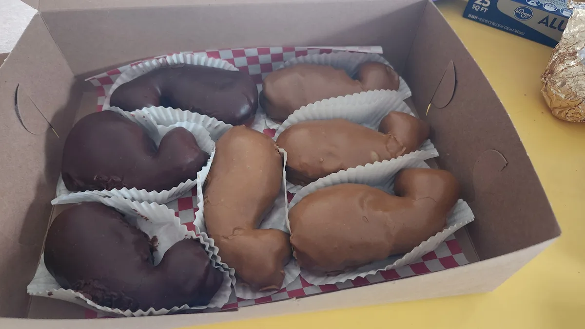 A cardboard box contains six chocolate-covered pastries shaped like kidneys, arranged in individual paper cups on…
