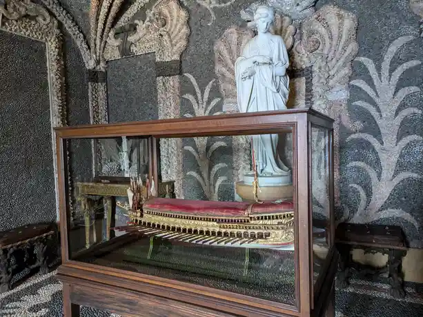 A detailed ornate boat model, resembling a galleon with red velvet seating and gold trim, is displayed inside a glass case…