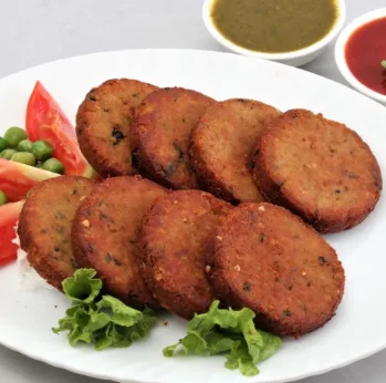 A white plate holds eight golden-brown, round, fried food items resembling patties or cutlets, garnished with lettuce…