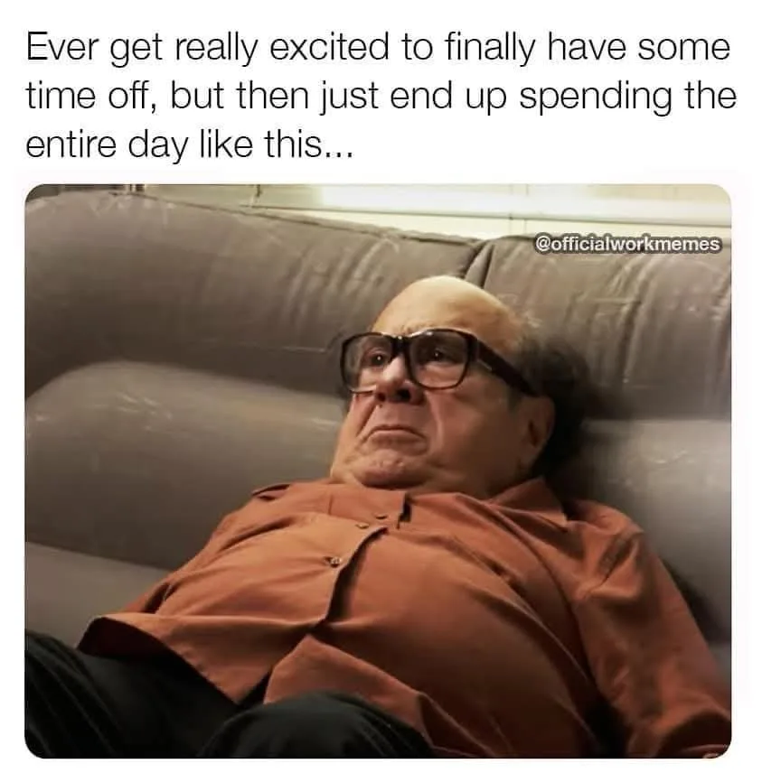 A man with thick-rimmed glasses and an orange button-up shirt lies on a gray couch, looking bored and unenthusiastic. The…