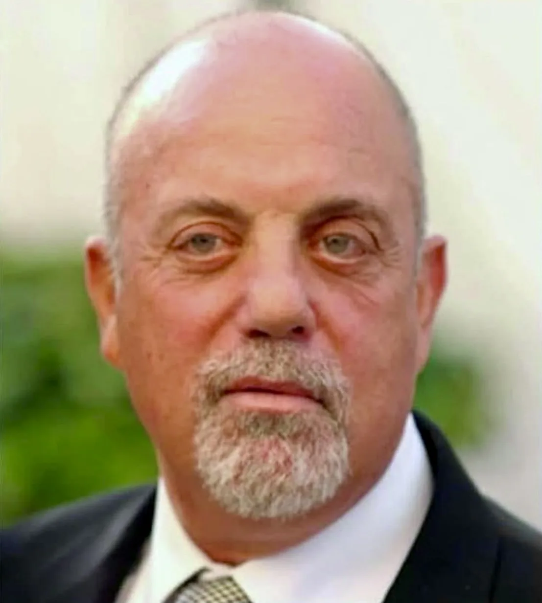 a close-up photo of a balding, middle-aged man with a gray goatee, wearing a dark suit, white shirt, and patterned tie…