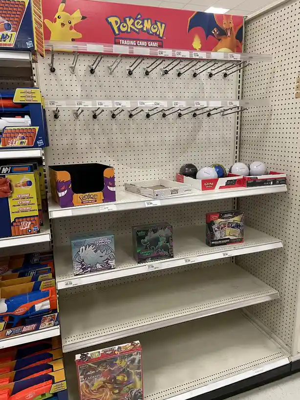 A retail aisle displays mostly empty shelves under a 'Pokémon Trading Card Game' sign, with only a few scattered booster…