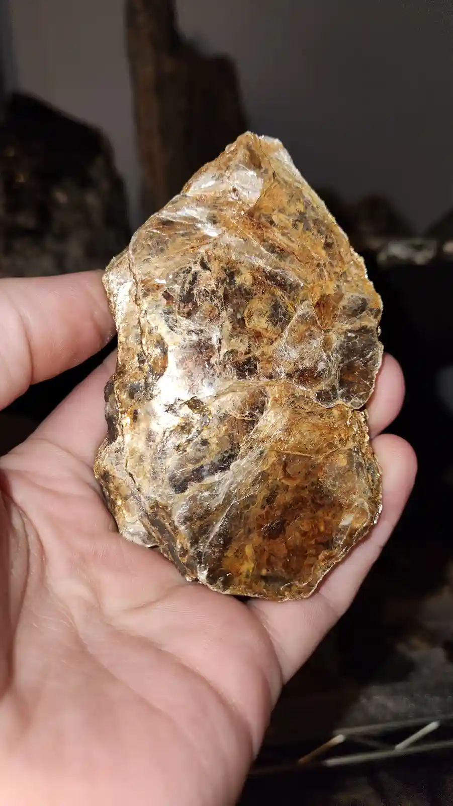 A hand holds a rough, translucent, golden-brown mineral specimen with visible internal fractures and inclusions, resembling…