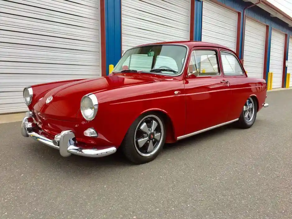 a shiny red classic car with chrome bumpers and modern-style wheels is parked in front of a building with white roll-up…