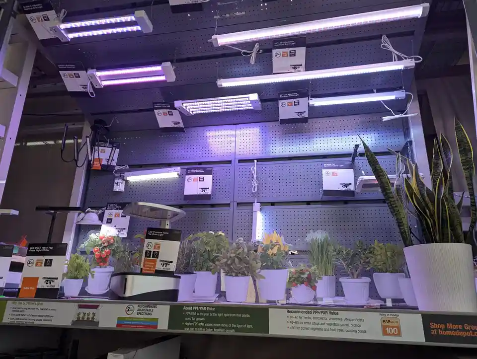 A retail display of LED grow lights hanging above potted plants in a store, with price tags and product information visible…