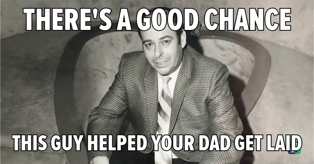 A black-and-white photo shows a man in a checkered suit and striped tie sitting in a curved chair, looking directly at the…