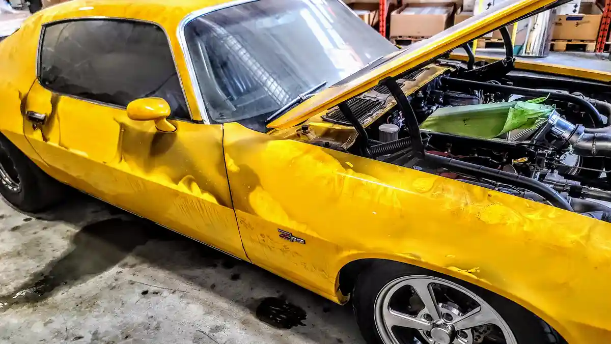 a bright yellow classic muscle car with its hood open sits in a garage, showing its engine. The car's body has visible…